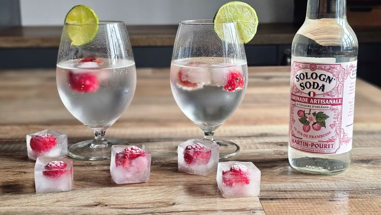 Deux verres de Sologn'Soda avec glaçons contenant des framboises fraîches.
